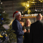 People in festive attire standing next to a Christmas tree in St Stradbroke Wine Bar