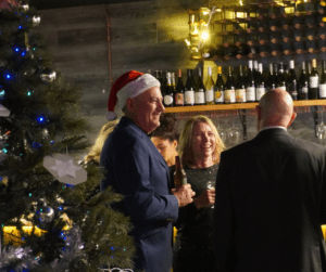 People in festive attire standing next to a Christmas tree in St Stradbroke Wine Bar
